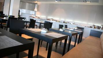 Um restaurante moderno com mesas comunitárias longas e uma área de cozinha ao fundo.