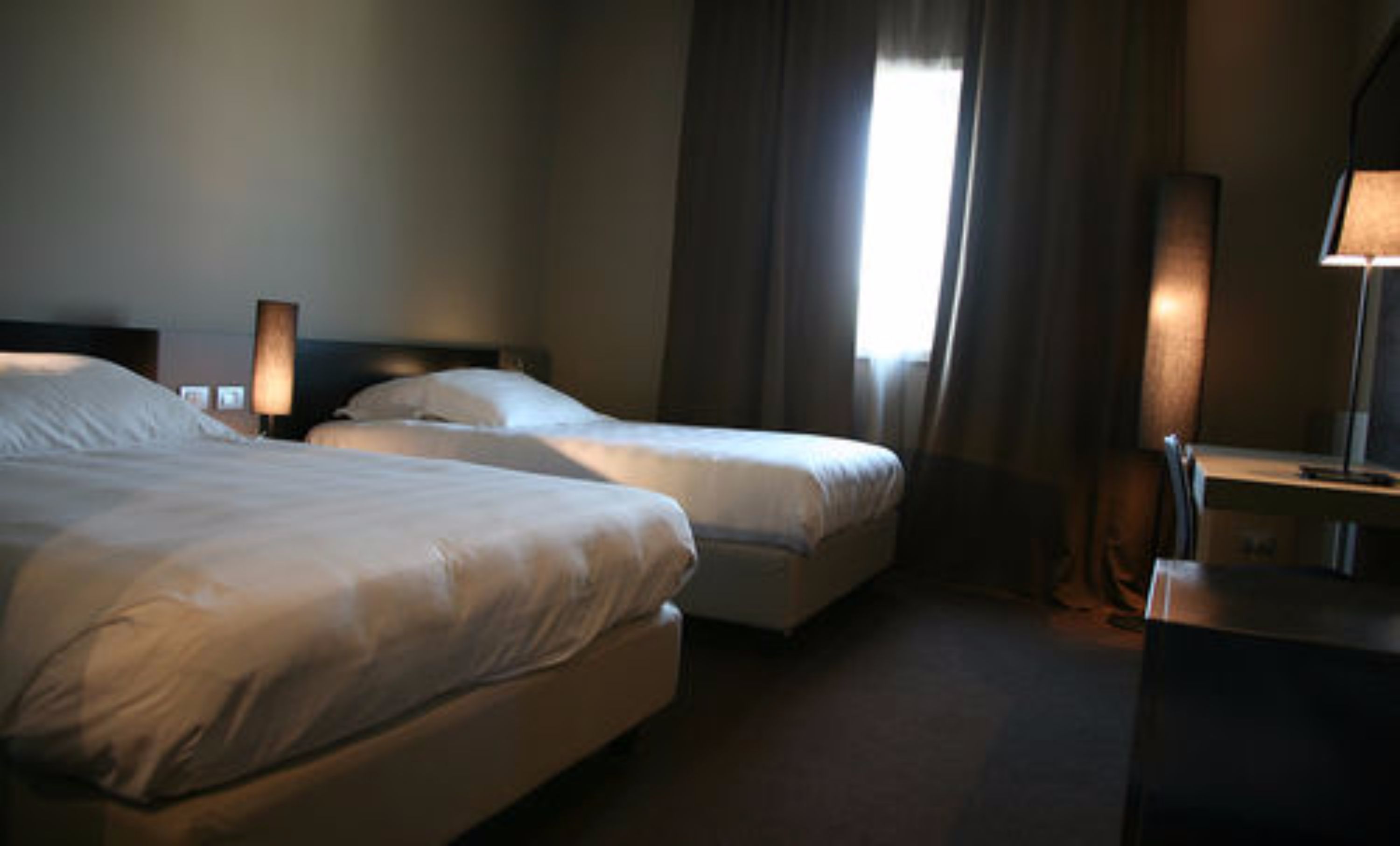 A hotel room with two beds, a desk with a lamp, and a window with curtains.