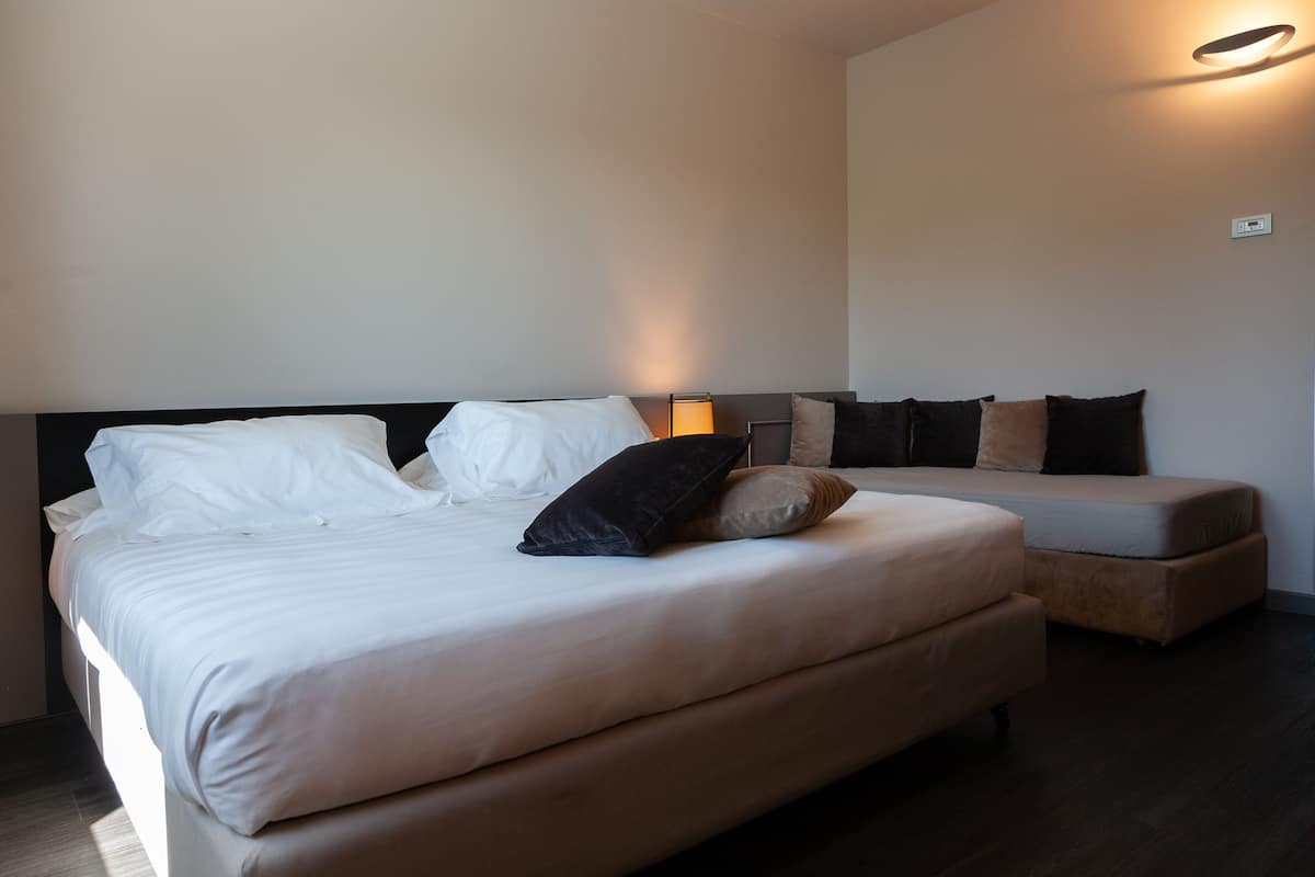 A modern hotel room with a large bed, a bedside table, a nightstand, and a wall-mounted light fixture.