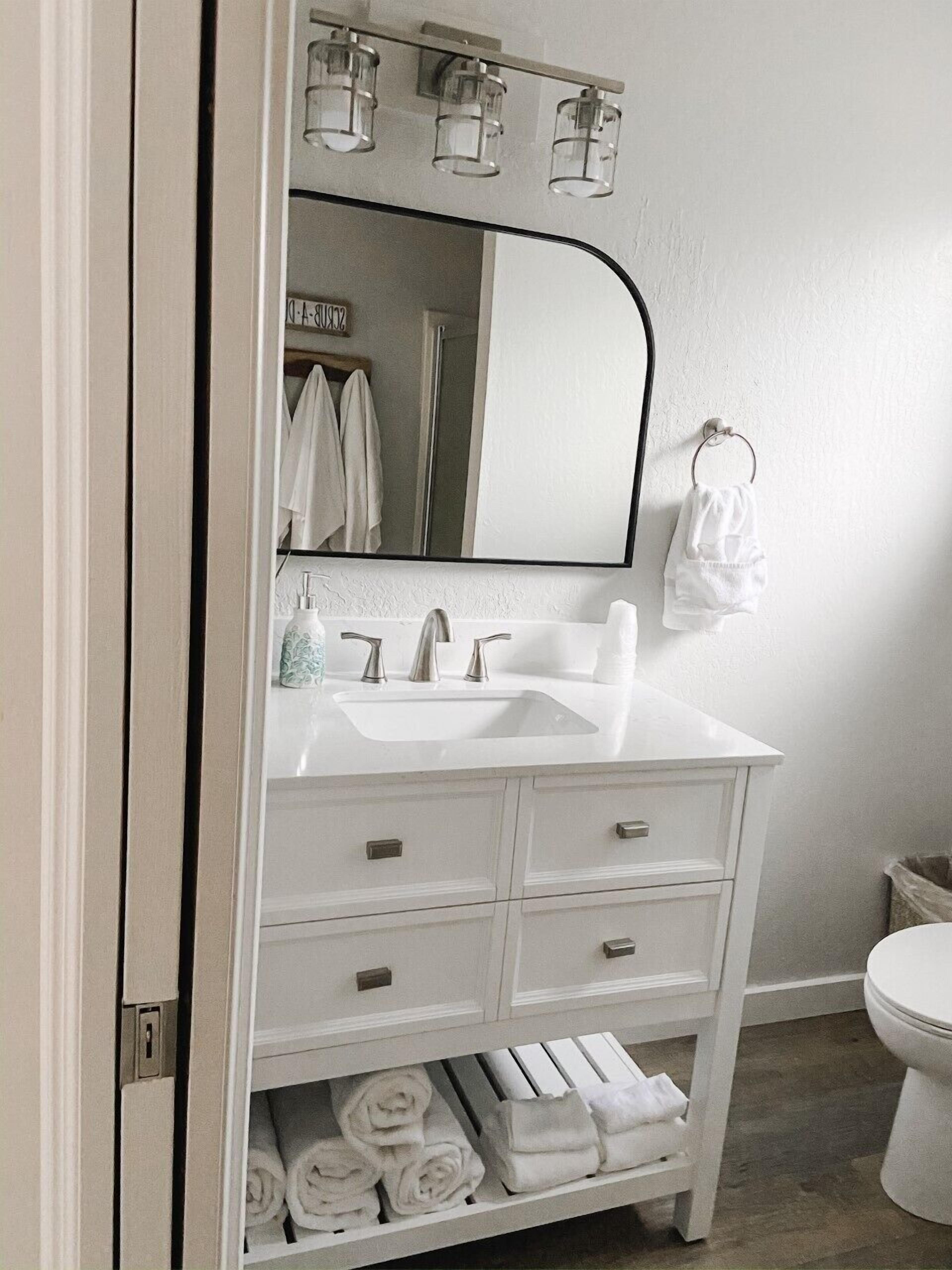 Une salle de bain avec un meuble-lavabo blanc, un miroir, un évier et des toilettes.