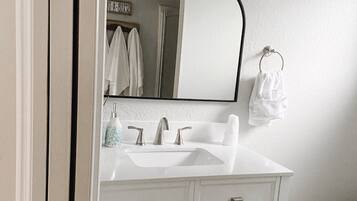 A bathroom with a white vanity, a sink, a mirror, and a toilet.