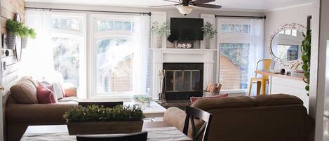 A cozy living room with a fireplace, a ceiling fan, and a television.