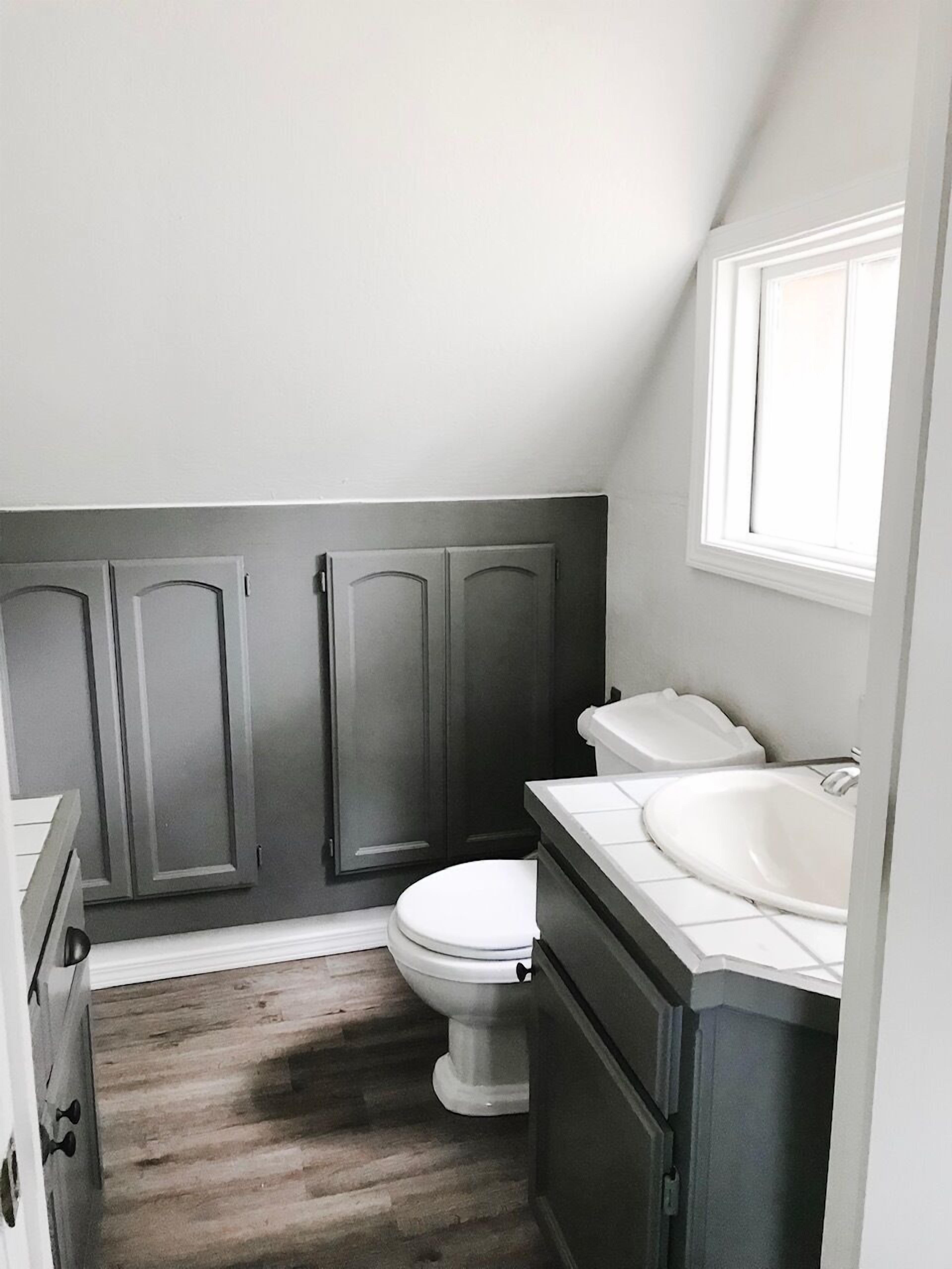 A small, compact bathroom with a toilet, sink, and dark wooden cabinets.