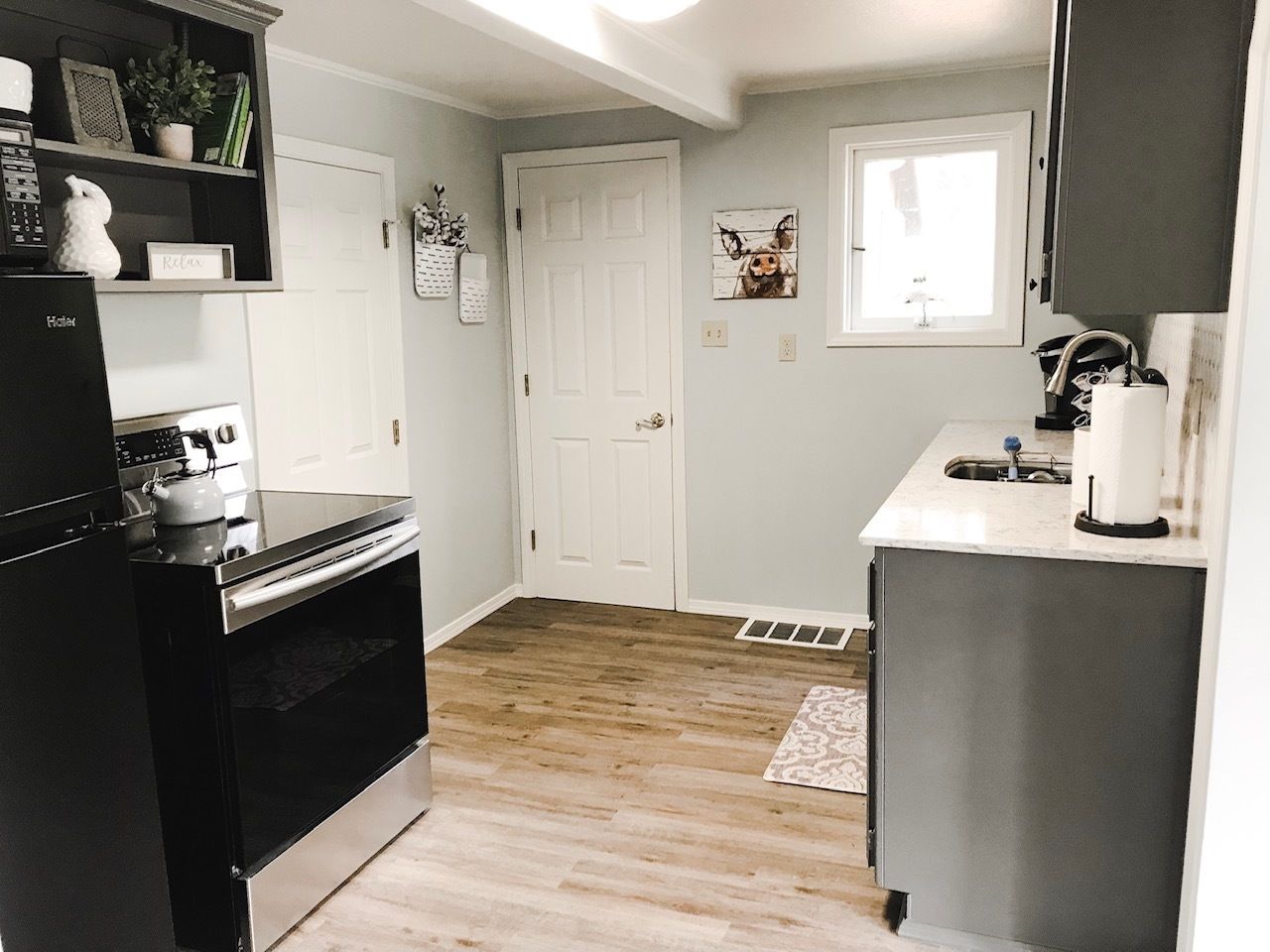 A compact kitchen with a black refrigerator, a stove, and a sink. There is a white door and a window with a view of the outside.