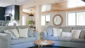 Ein modernes Wohnzimmer mit zwei grauen Sofas, einem Holztisch und einer Küche im Hintergrund.