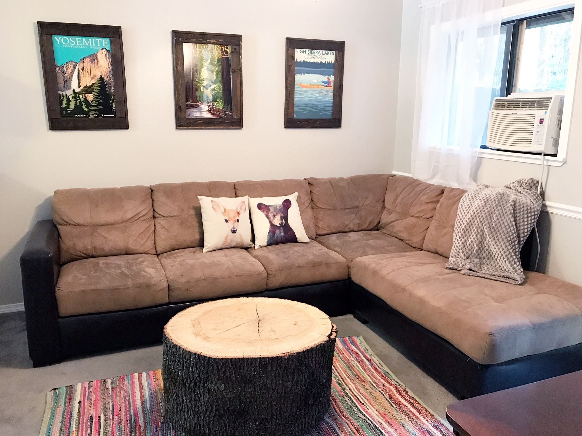 Ein Wohnzimmer mit einem braunen Ecksofa, zwei Kissen mit Tiermotiven, einem Holzboden und drei gerahmten Postern an der Wand.