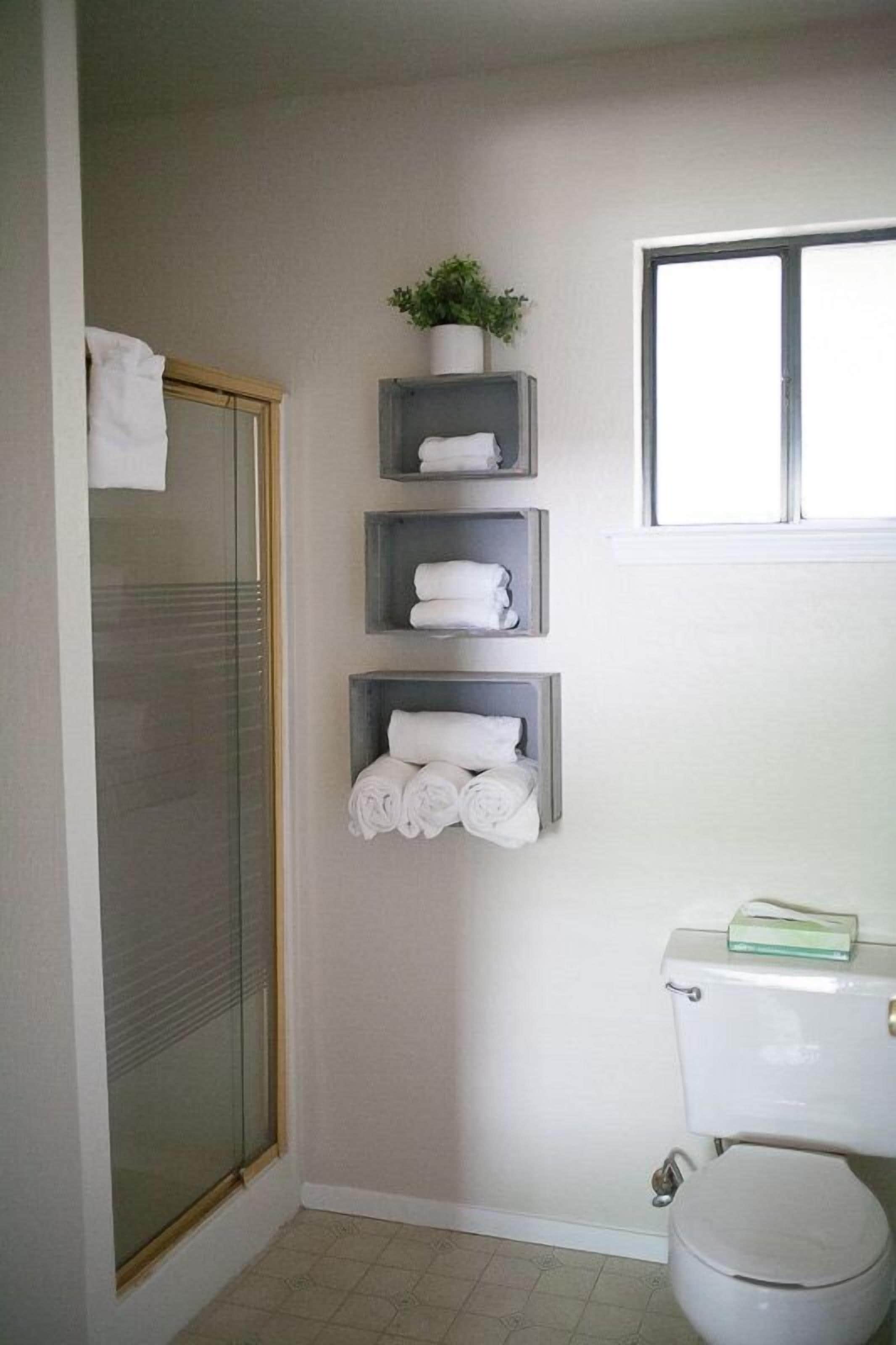 A bathroom with a glass shower door, a toilet, and three shelves with towels.