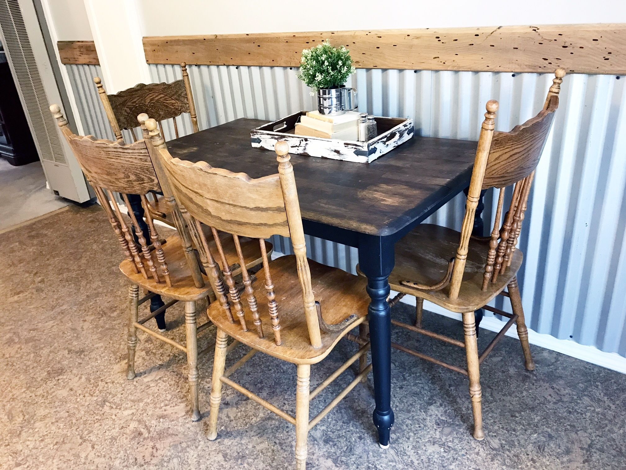 A dining table with four wooden chairs, a tray with a plant, and a metal pitcher on the table.