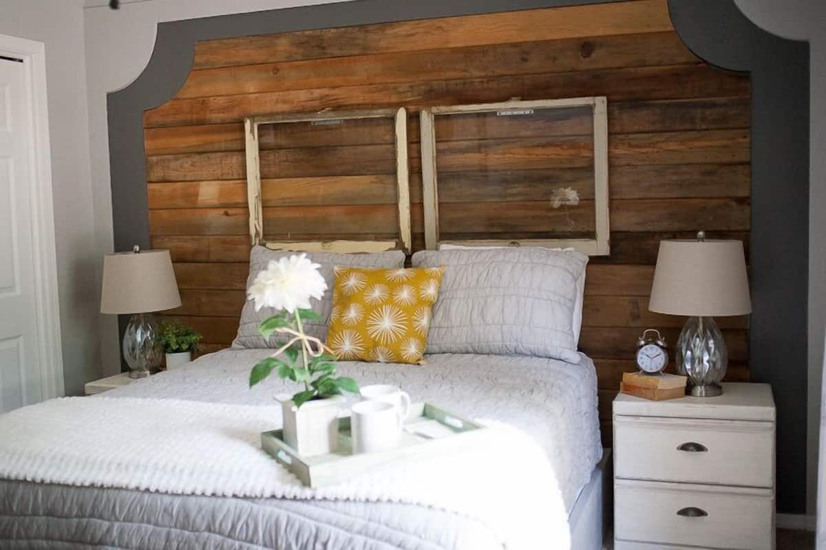 A bedroom with a wooden headboard, a bed with white bedding, two bedside lamps, and a nightstand with a clock and a tray of items.