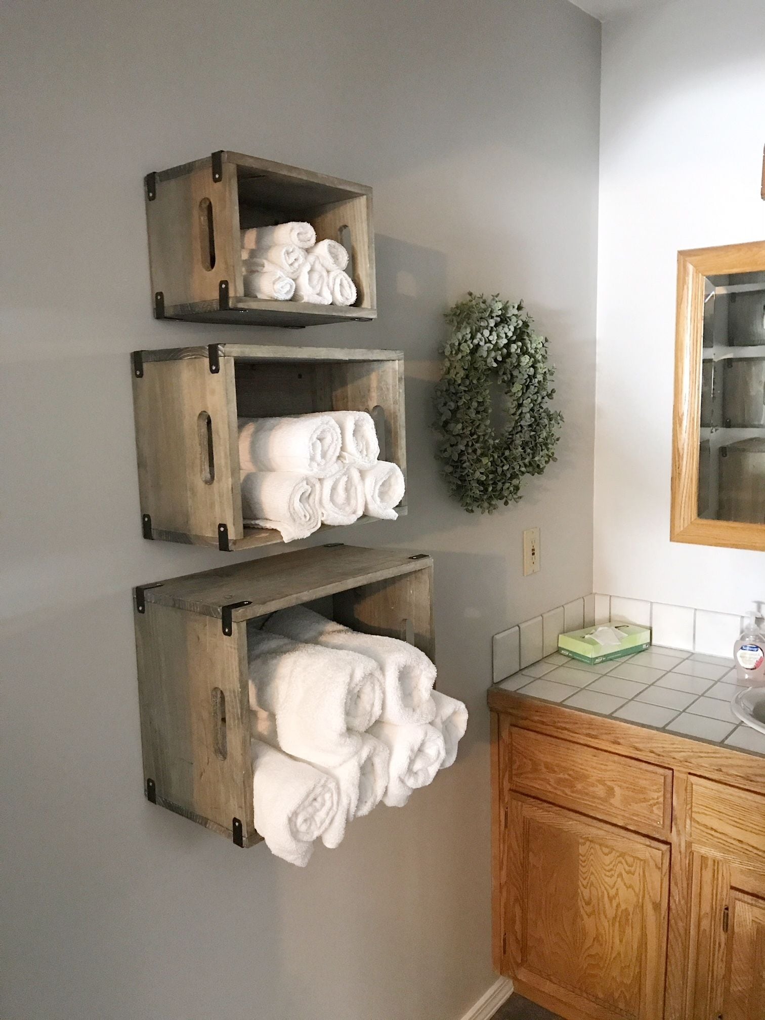 Ein Badezimmer mit hölzernen Handtuchhaltern, die weiße Handtücher tragen, einem grünen Kranz an der Wand und einem Holzkabinet mit einem Spiegel.