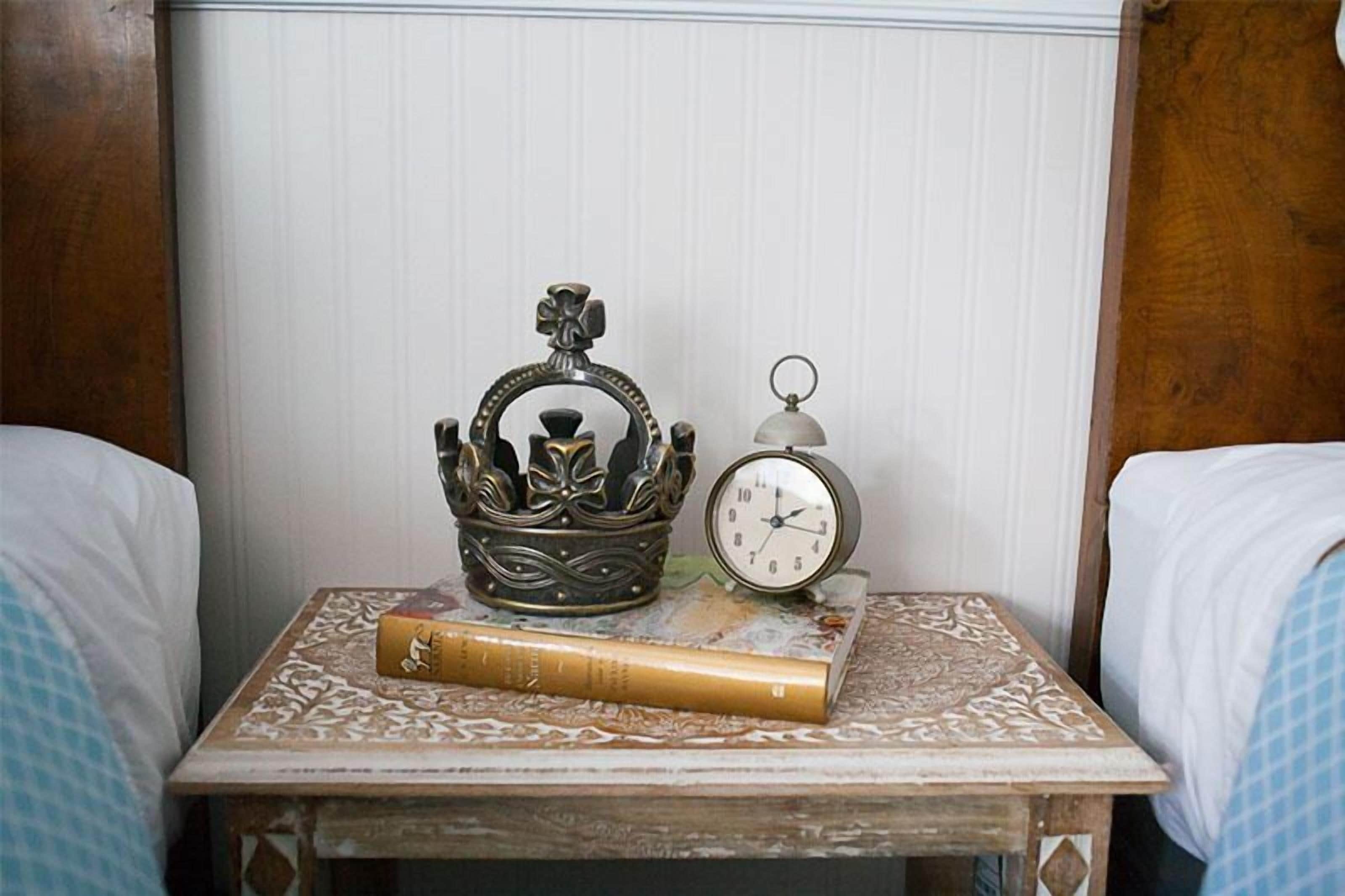 A small bedside table with a decorative metal crown, a classic alarm clock, and a book.