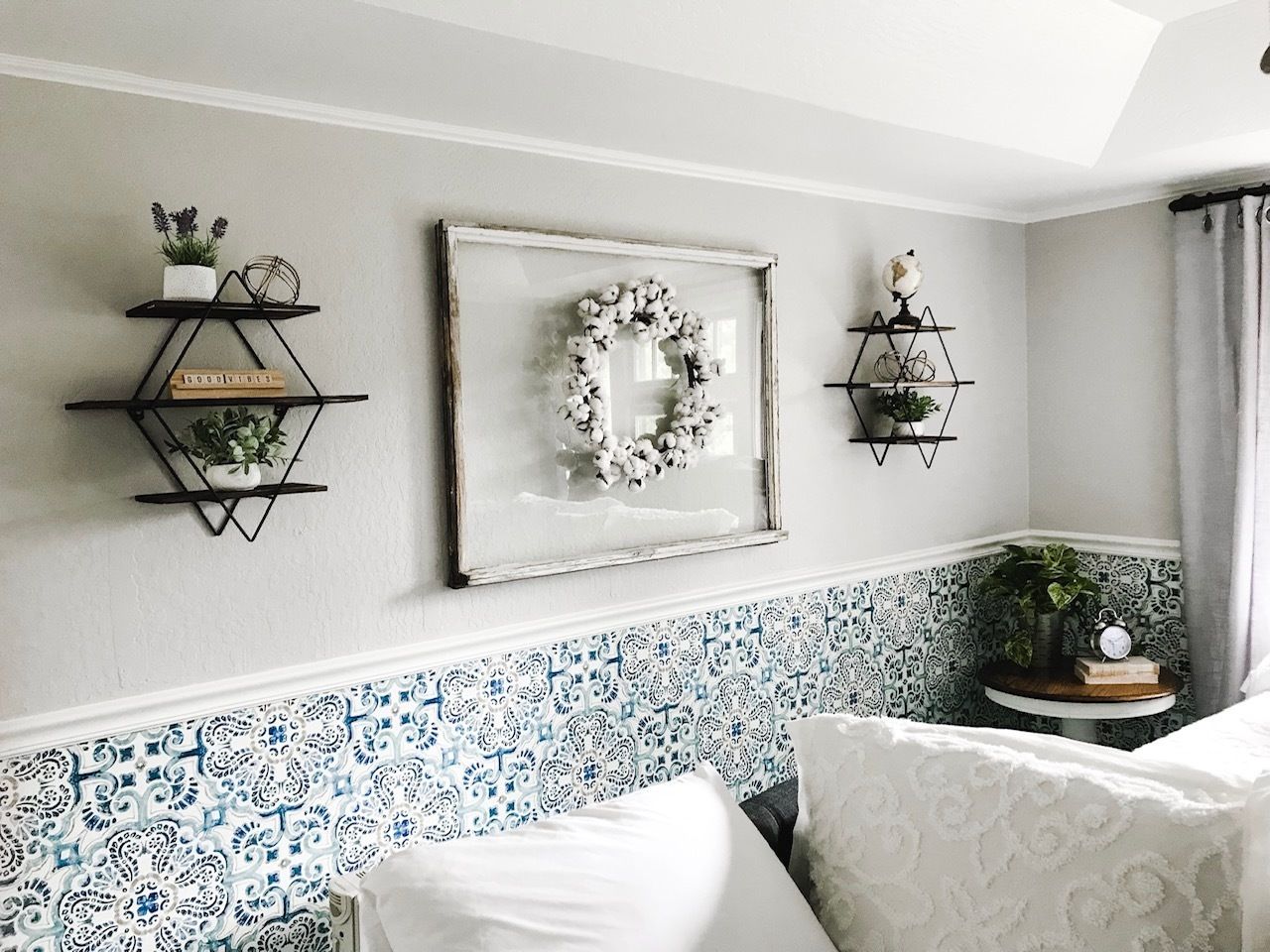 A bedroom with a patterned tile border, a white bed, and three wall-mounted shelves with decorative items.