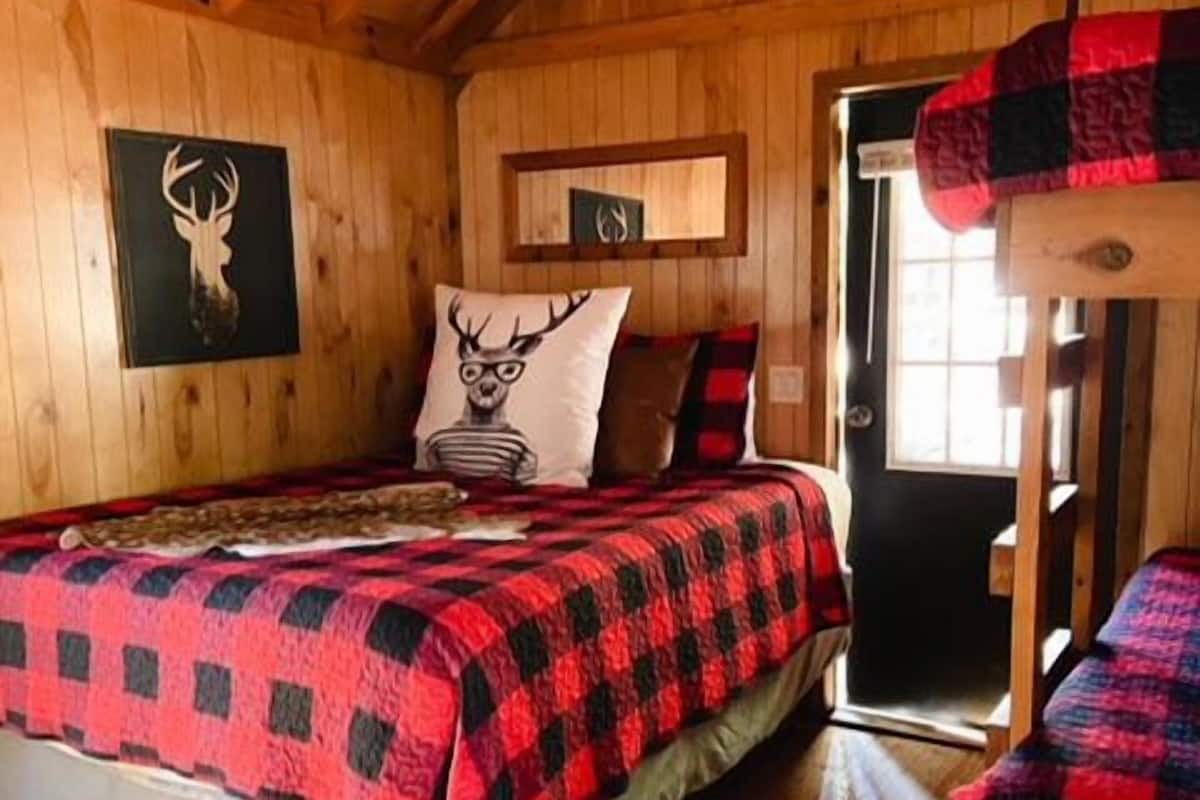 A cozy cabin-style bedroom with a bed, a wooden ceiling, a deer head wall decoration, and a door.
