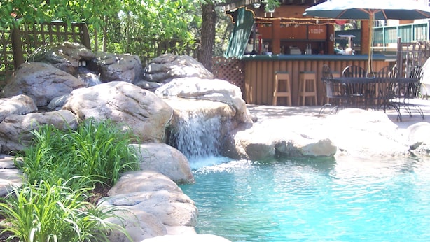 Ein Poolbereich mit Felsen, einem Wasserfall und Sitzmöglichkeiten im Freien.