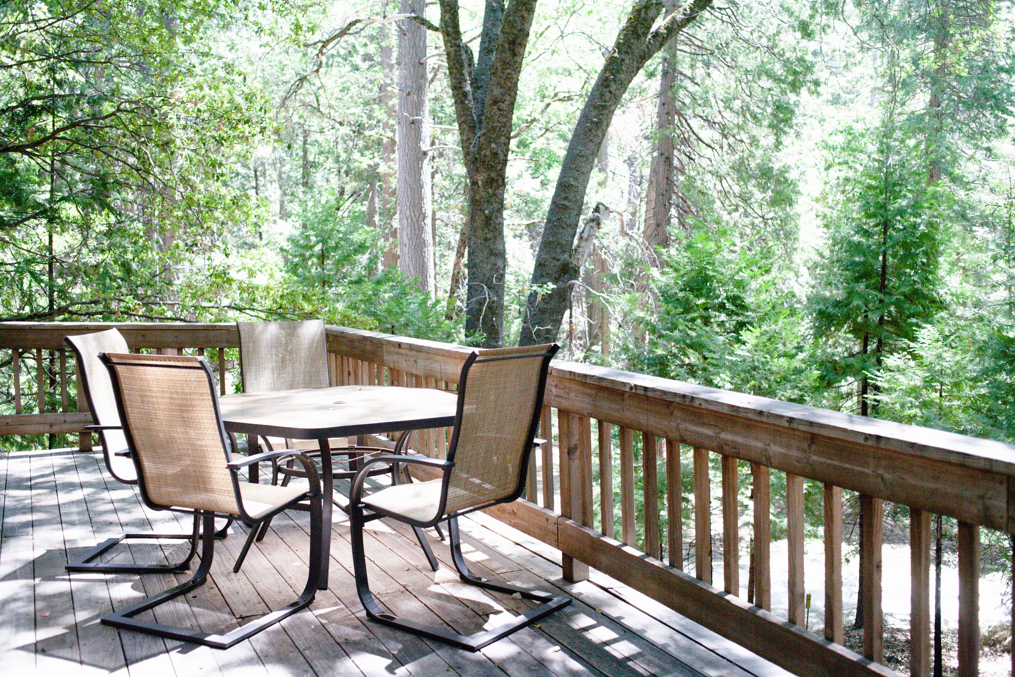 A wooden deck with a table and chairs, surrounded by trees.