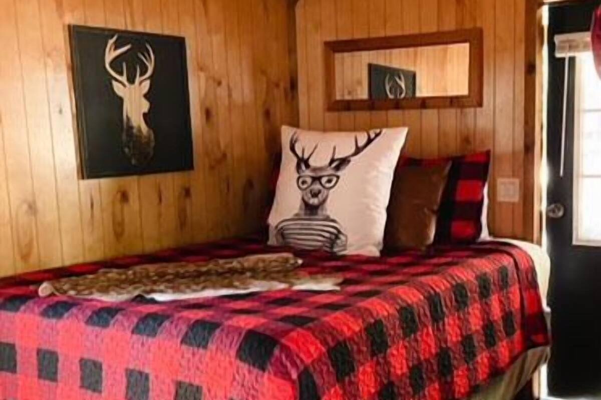 A wooden cabin bedroom with a bed, a deer wall art, and a shelf with antlers.
