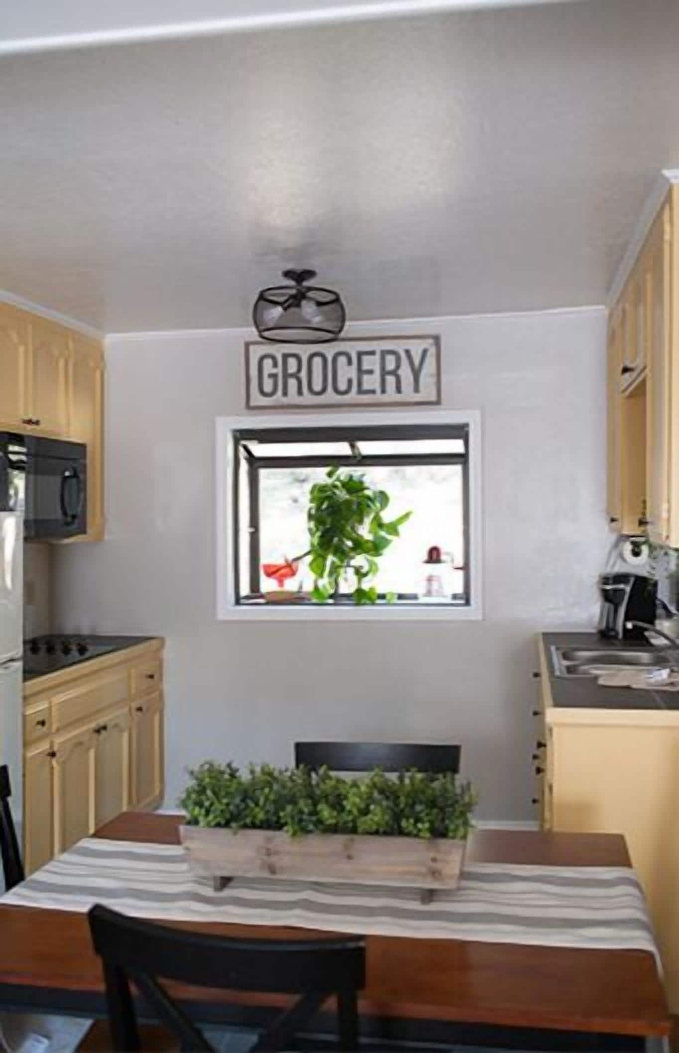 Una cocina con ventanal, un cartel que dice 'GROCERY' y una mesa con sillas.