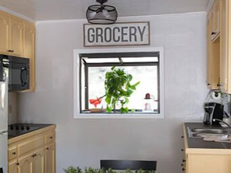 Una cocina con ventanal, un cartel que dice 'GROCERY' y una mesa con sillas.