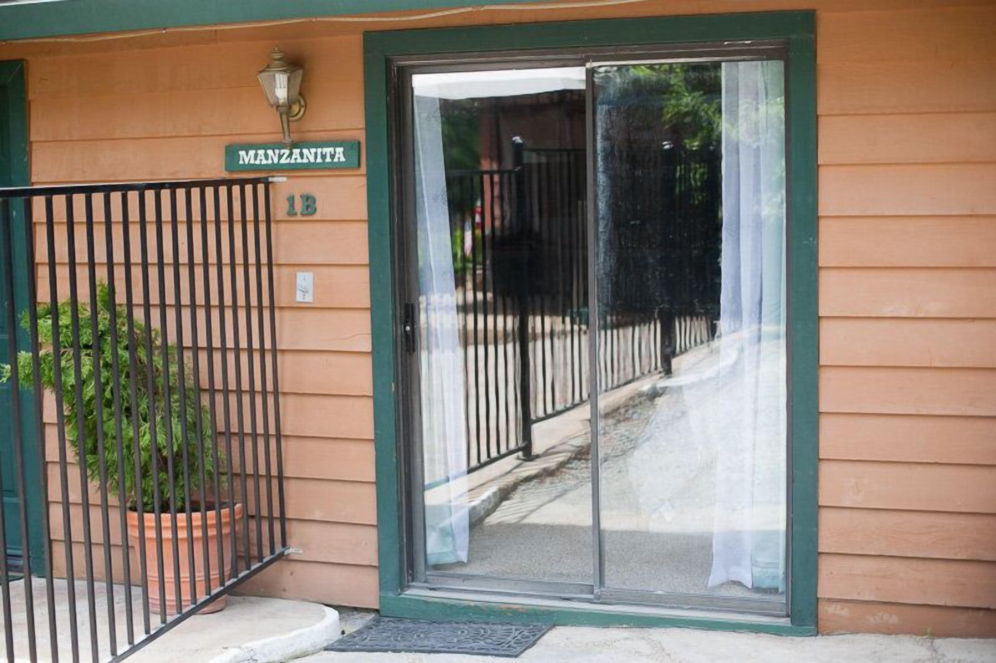 A building entrance with a sliding glass door, a metal gate, and a potted plant.