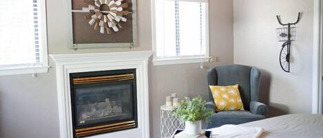 A cozy room with a fireplace, a chair, a bike rack, and a window with blinds.
