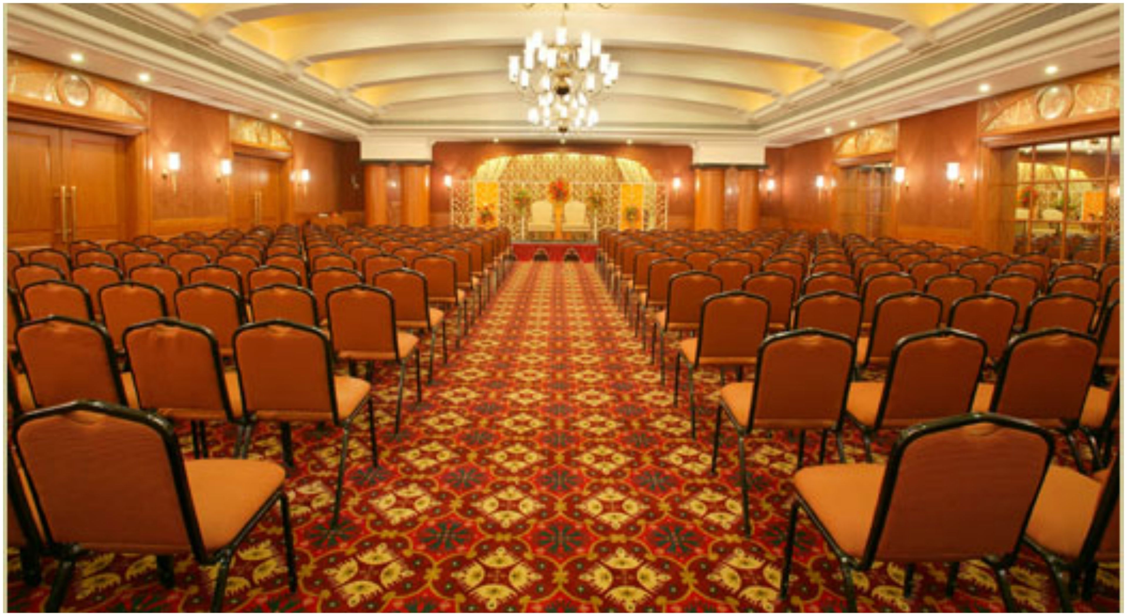 Un salón de conferencias con filas de sillas, una alfombra estampada y una araña.