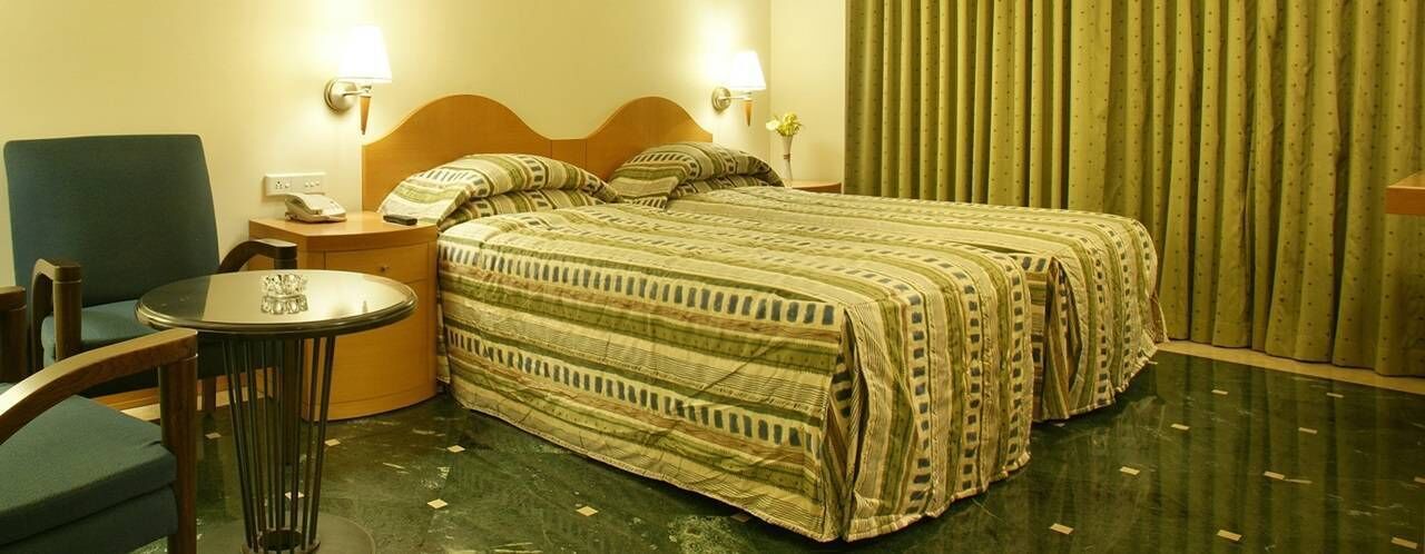 Una habitación de hotel con una cama, dos mesitas de noche, una silla y una pequeña mesa.