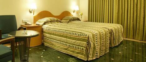 Una habitación de hotel con una cama, dos mesitas de noche, una silla y una pequeña mesa.