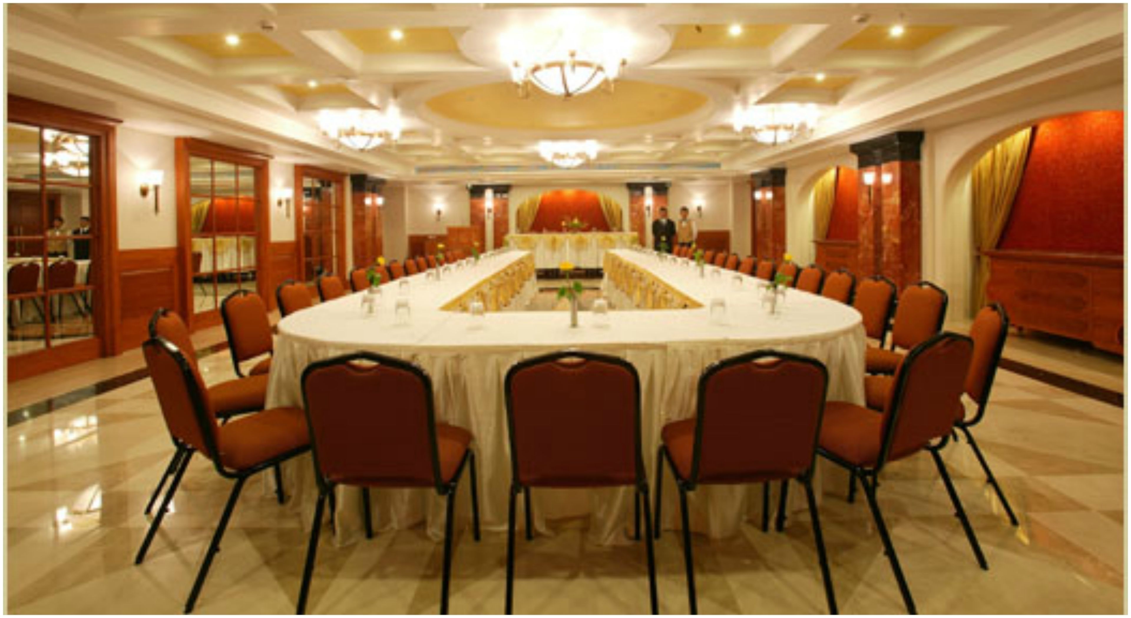 Een ruime congreszaal met een ronde tafel, stoelen en een kroonluchter.