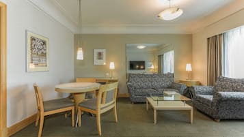 Habitación de hotel con una mesa de comedor, dos sillas, un sofá, una mesa de centro y un televisor al fondo.