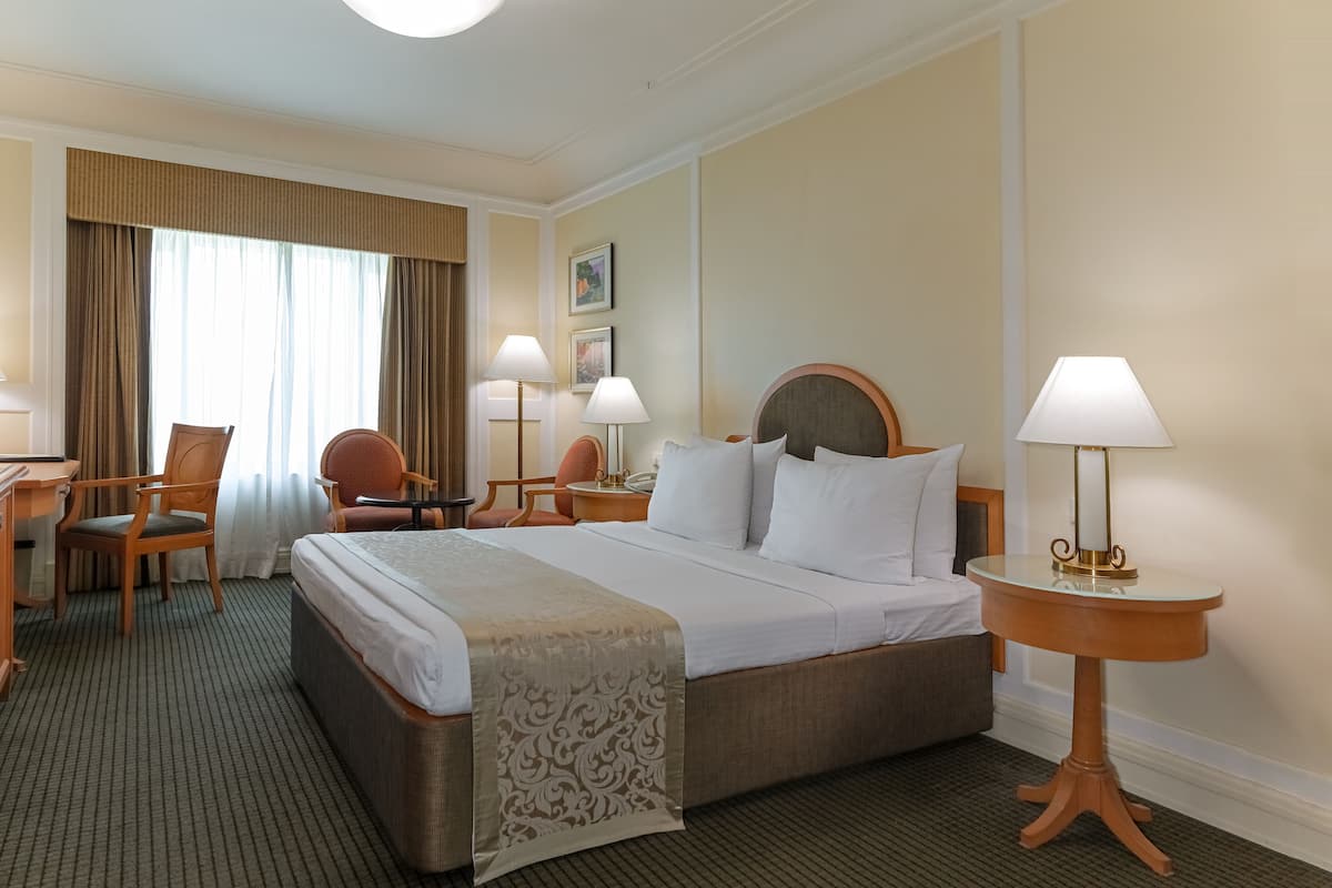 Ein Hotelzimmer mit einem großen Bett, zwei Nachttischen, einem Schreibtisch, einem Stuhl und einer Lampe.