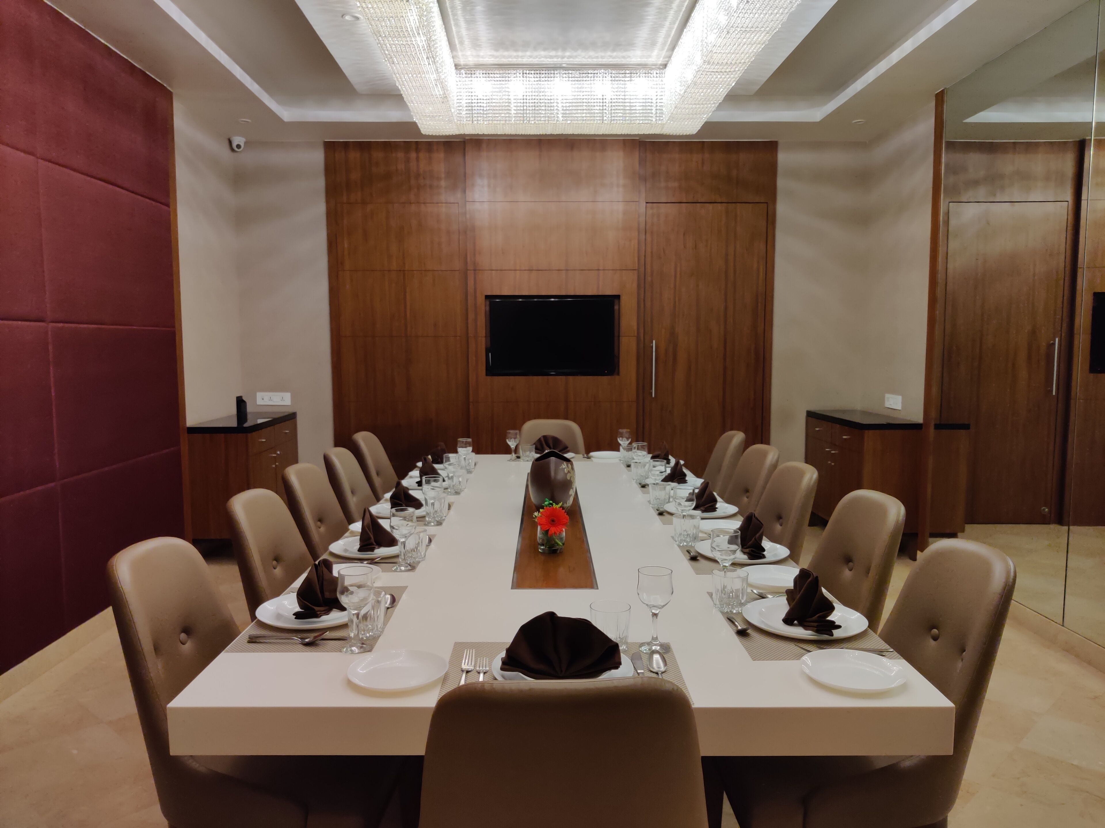 Une salle de conférence avec une longue table préparée pour une réunion, équipée de chaises, d’assiettes, de verres et agrémentée d’un arrangement floral au centre.
