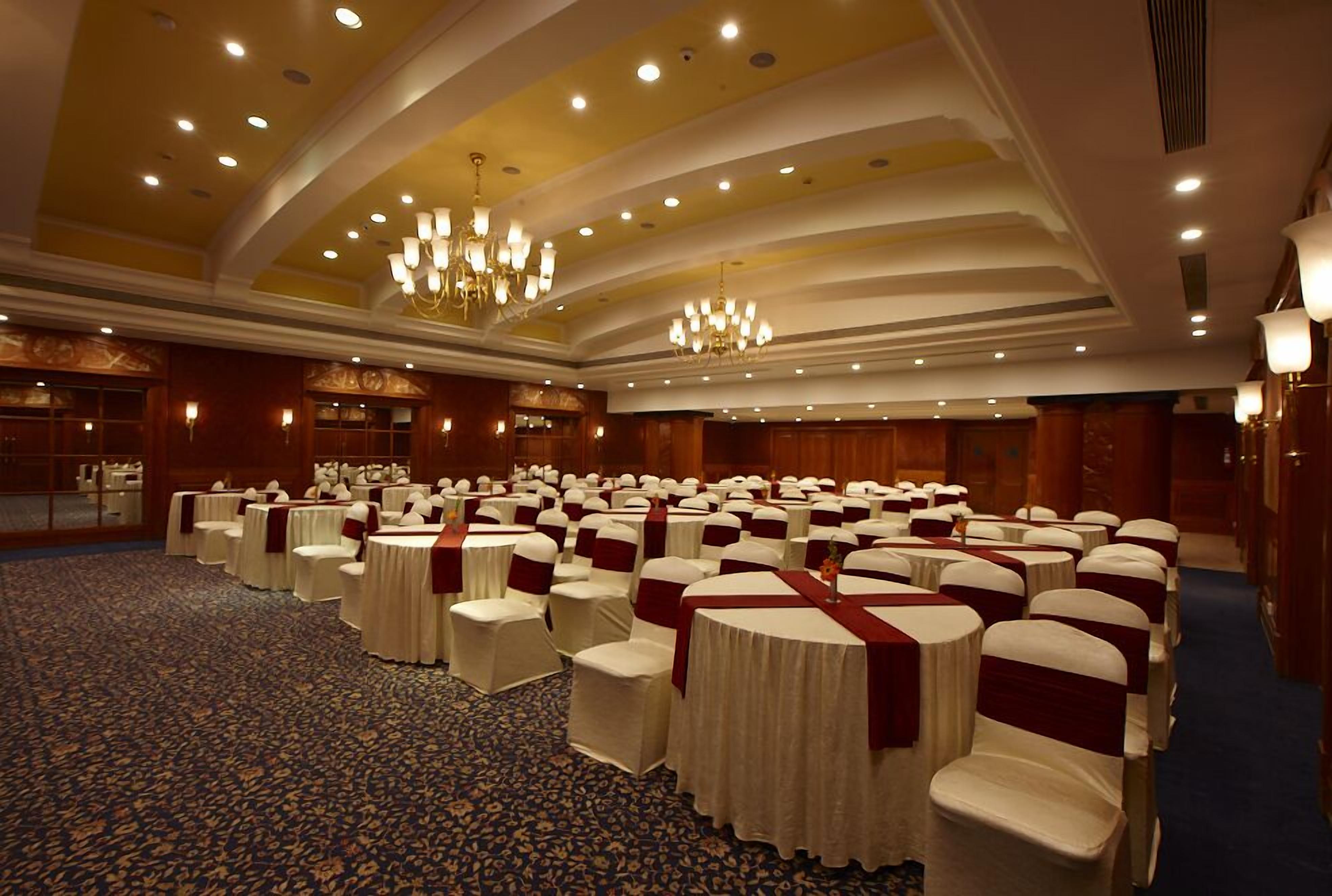 A large conference room with rows of round tables and chairs, each with white tablecloths and red sashes.