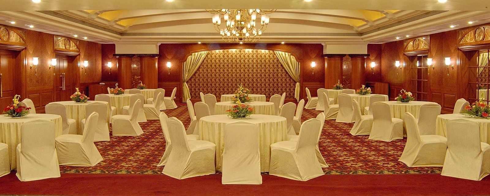 A banquet hall with round tables, white chairs, and a red carpet.