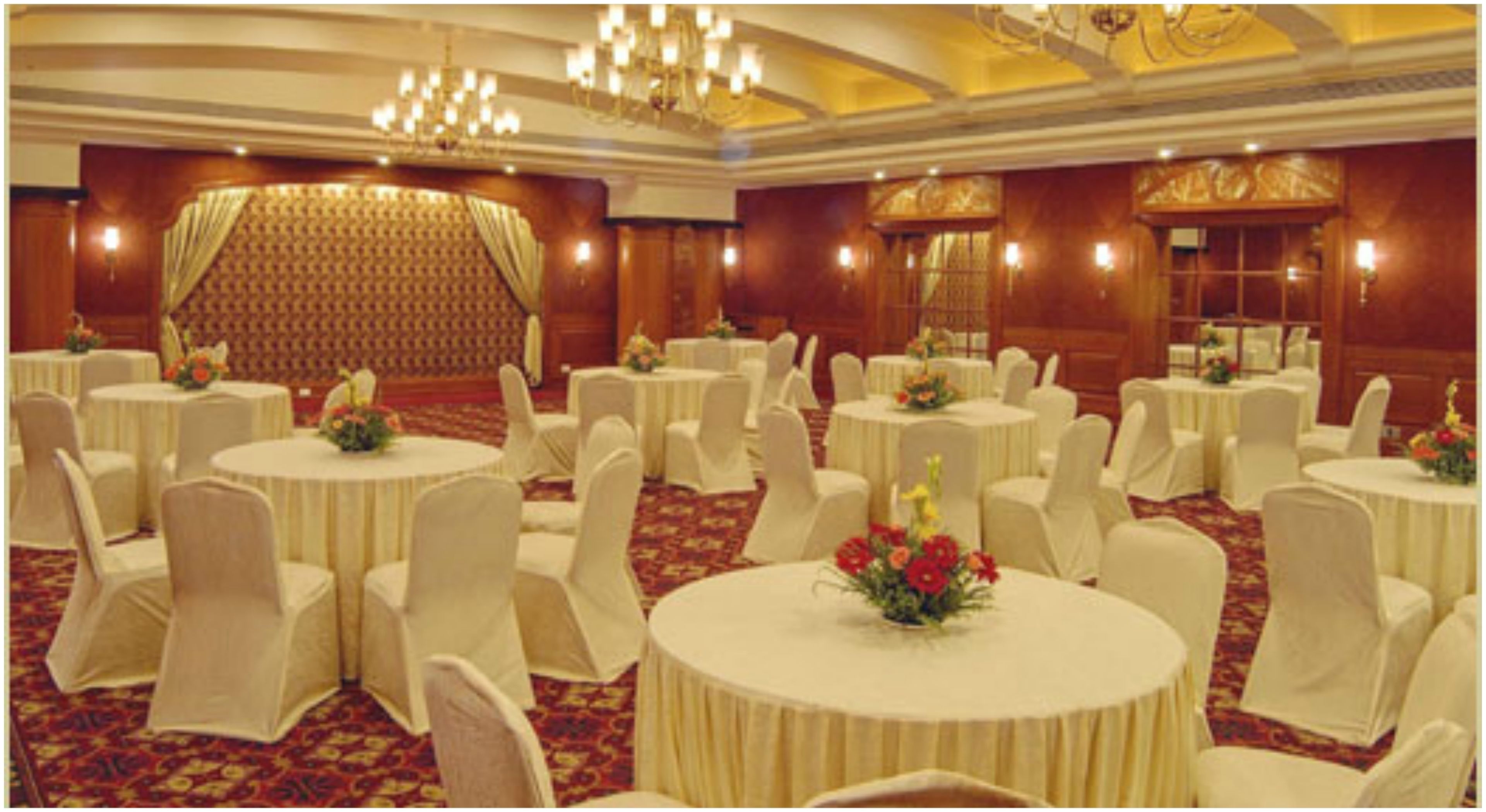 Un salón de banquetes con mesas redondas, sillas blancas y candelabros.