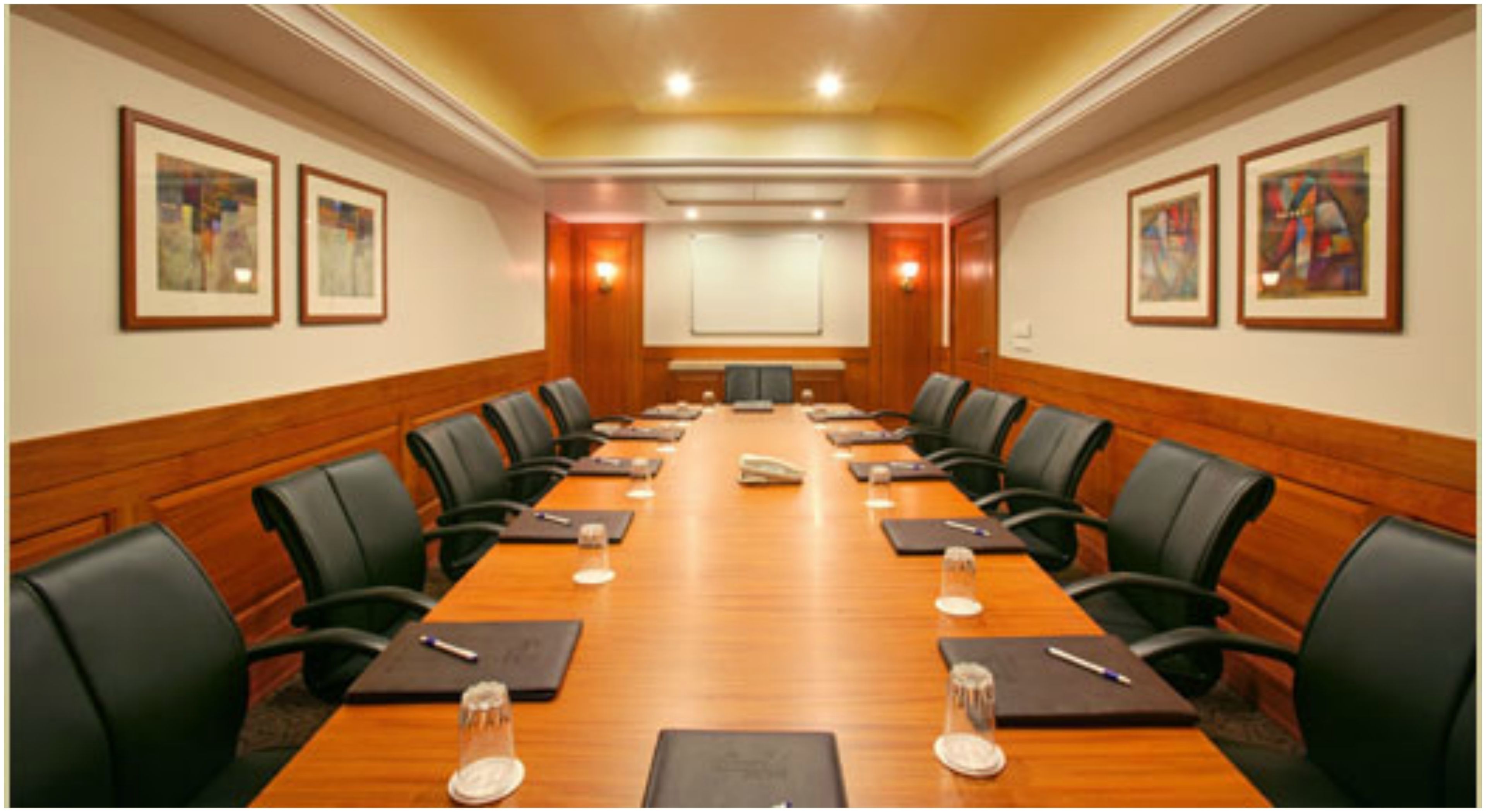 A conference room with a long table, black chairs, and framed artwork on the walls.