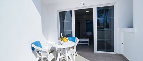 A white balcony with a table and chairs, a bottle of wine, and a bowl of fruit.
