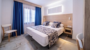 Ein modernes Hotelzimmer mit einem großen Bett, einem Nachttisch, einem Sessel und einem Fenster mit blauen Vorhängen.