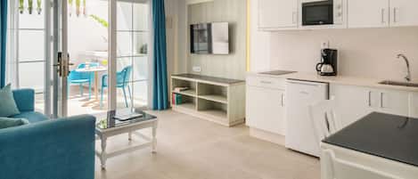 A modern kitchen with white cabinets, a microwave, and a coffee maker. There is a dining area with a table and chairs, and a sofa in the living room.