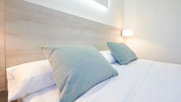 Een net opgemaakt bed met witte en lichtblauwe kussens, een houten hoofdbord en een wandlamp.