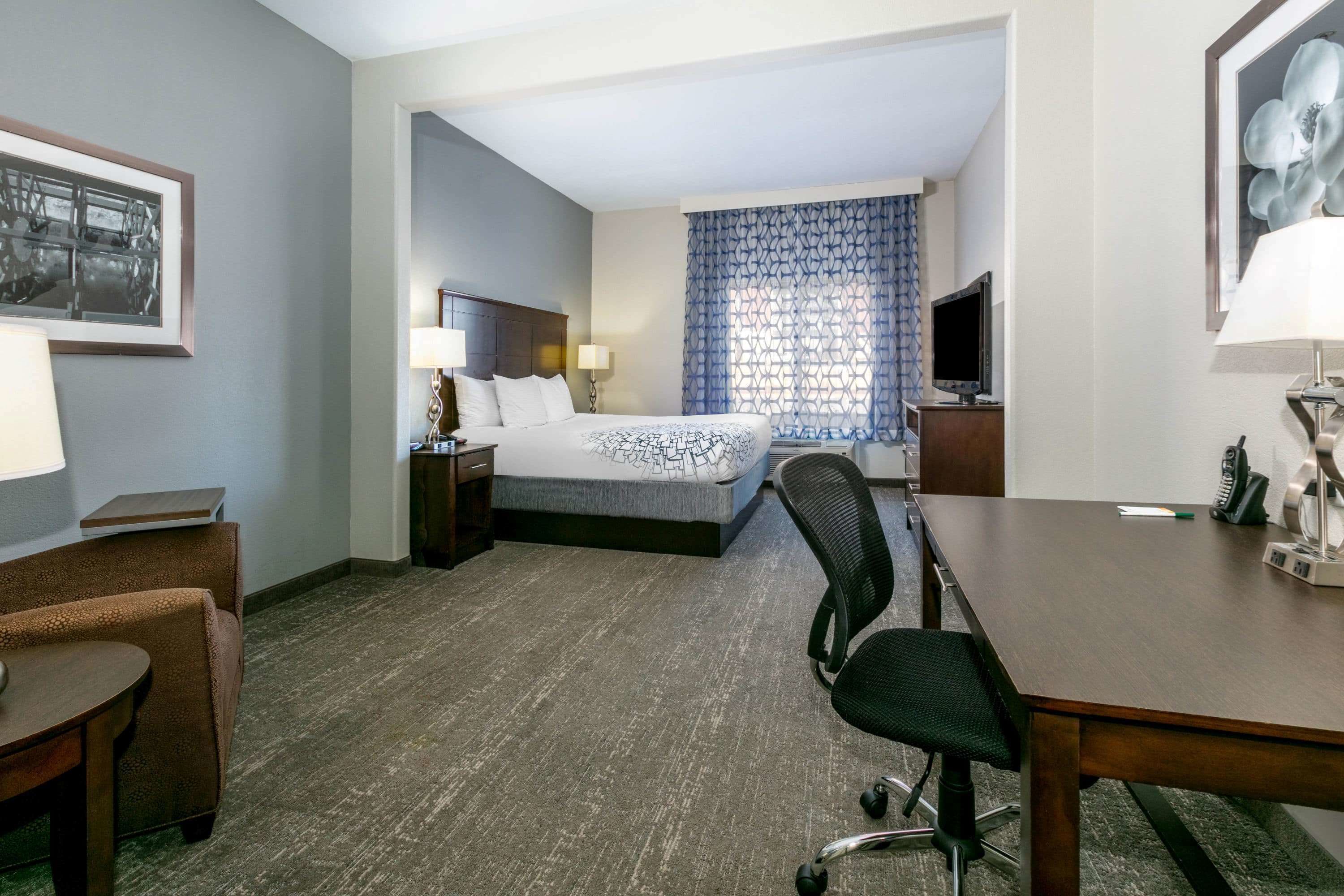 A hotel room with a bed, a desk, a chair, a TV, and a lamp.