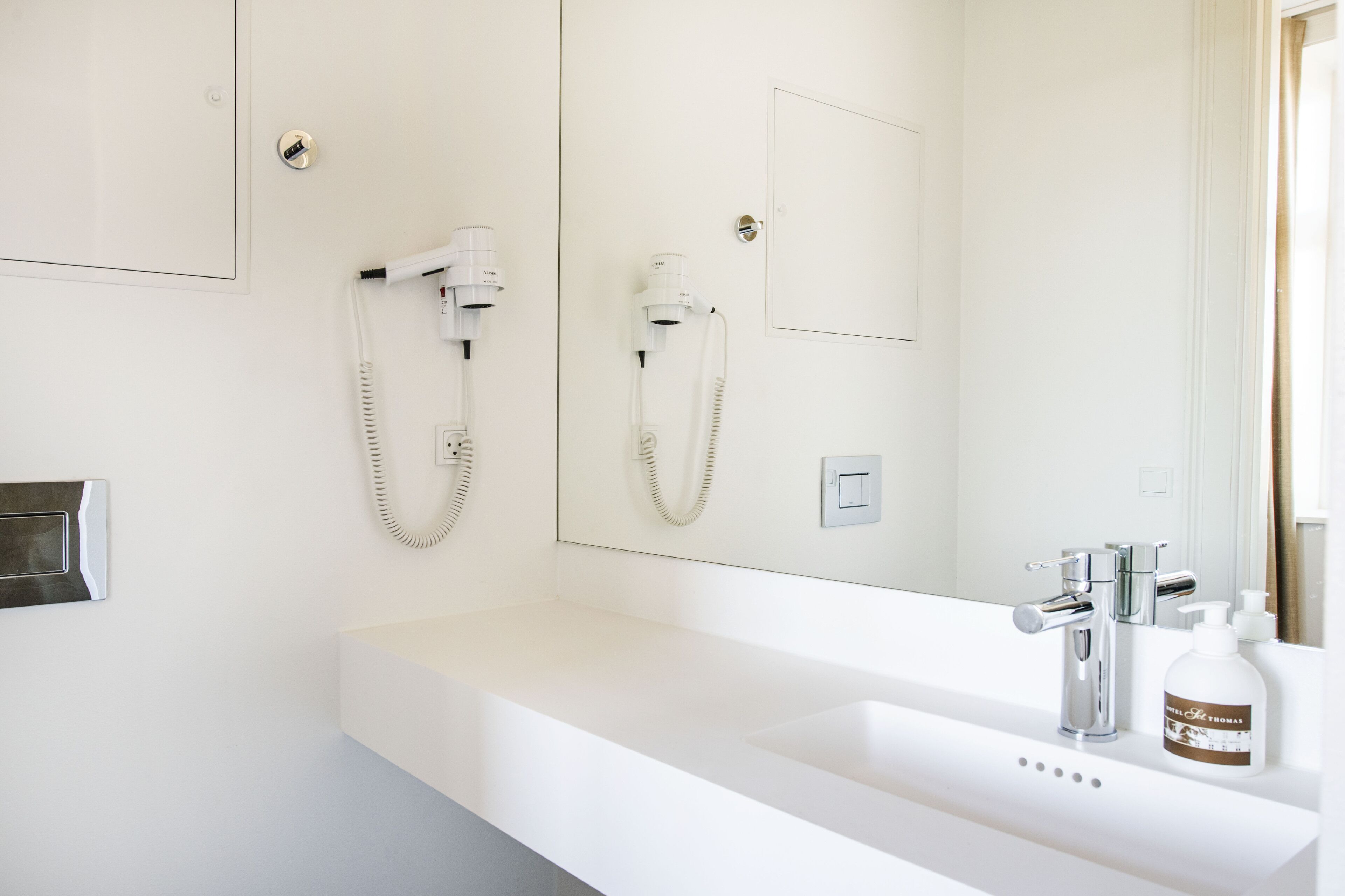 A modern bathroom with a white sink, a mirror, a handheld showerhead, and a bottle of soap.