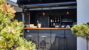Un área de bar al aire libre con mostrador, taburetes y una variedad de botellas y vasos.