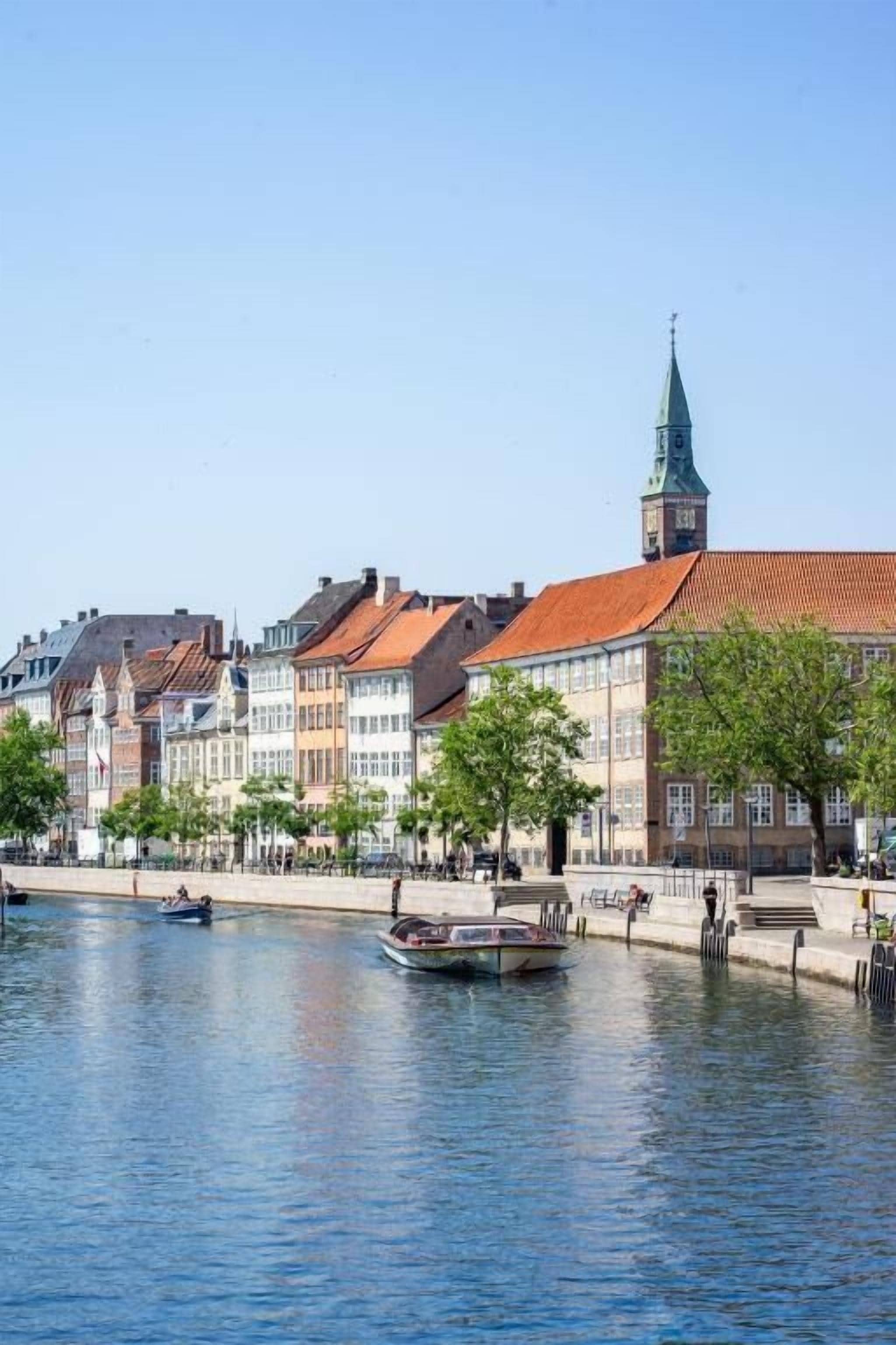 A canal with buildings on one side and a church steeple in the distance.