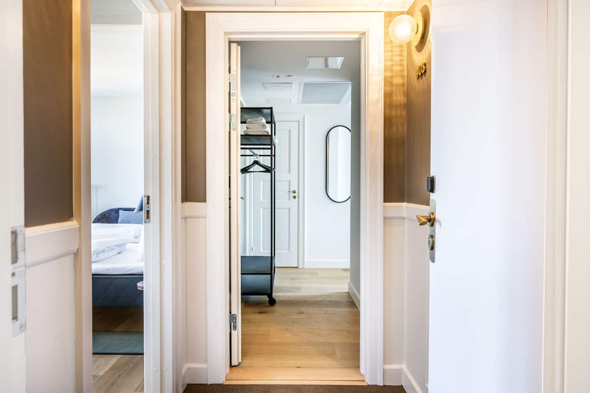 Um corredor leva a um quarto com uma cama, cômoda e espelho.