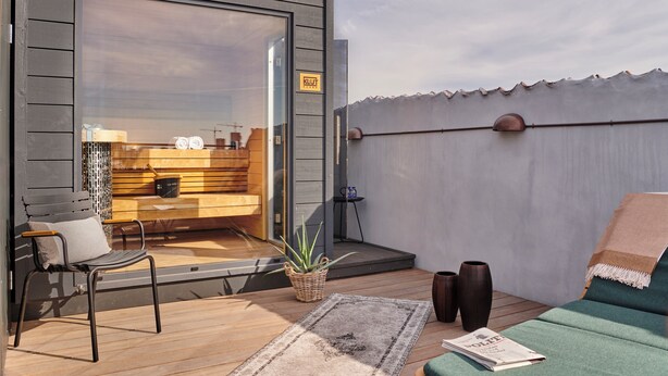 Un patio moderno al aire libre con terraza de madera, un banco acolchado, una mesita y una planta en maceta.