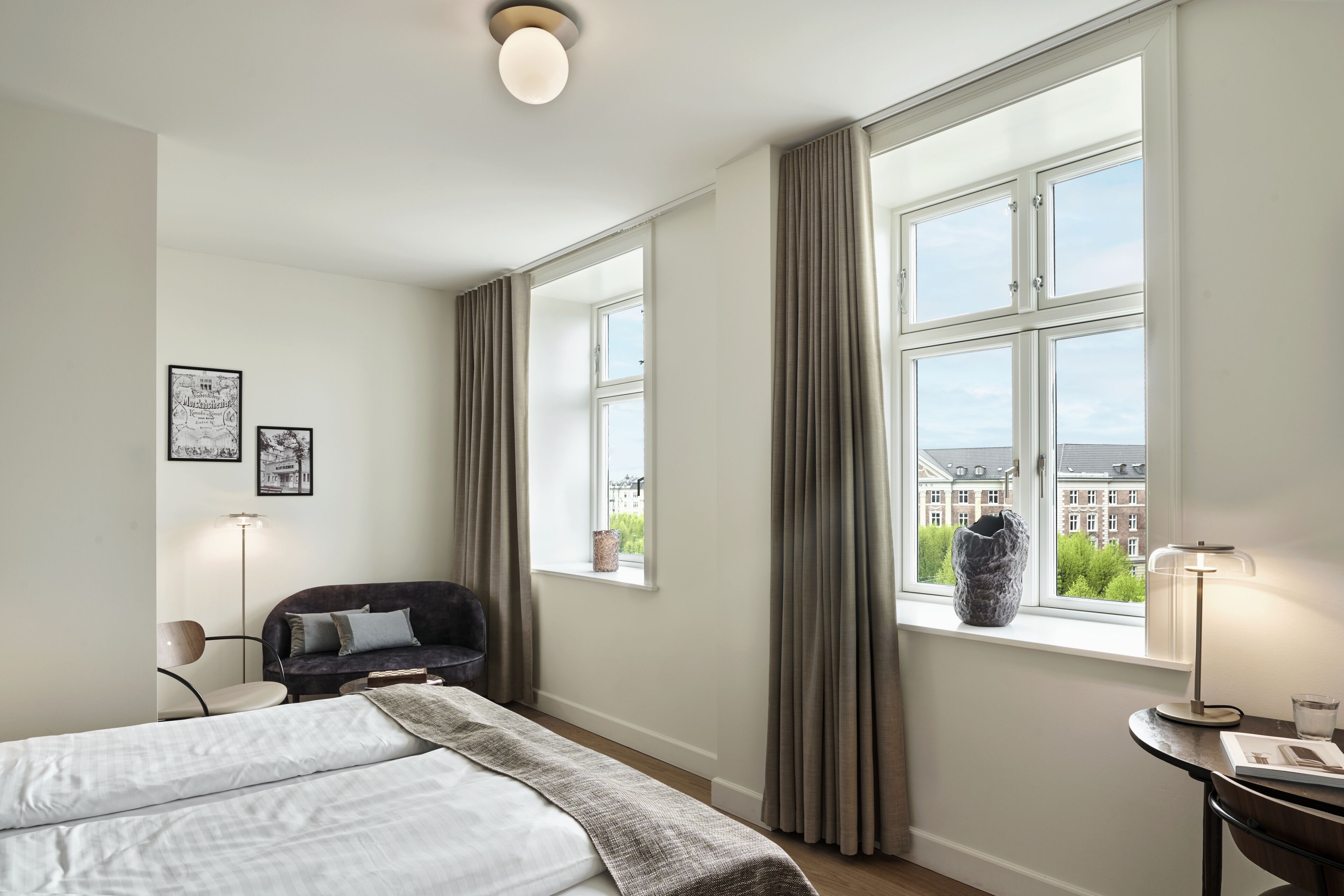 A hotel room with a bed, a desk, a chair, a lamp, and a window with curtains.