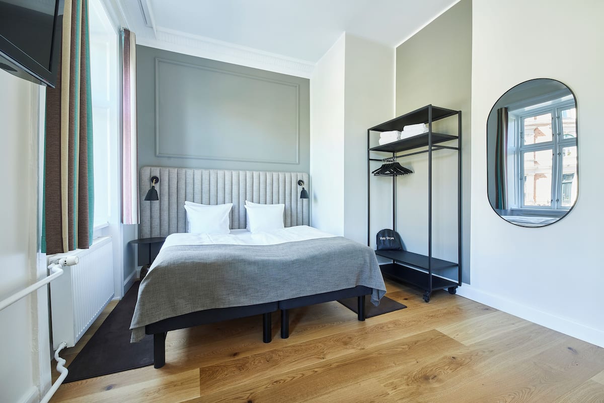 Quarto de hotel moderno com cama, mesas de cabeceira, guarda-roupa e um espelho grande.