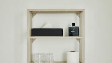 Una estantería con una caja negra, un frasco de perfume Chanel, dos recipientes de vidrio y un rollo de papel higiénico.