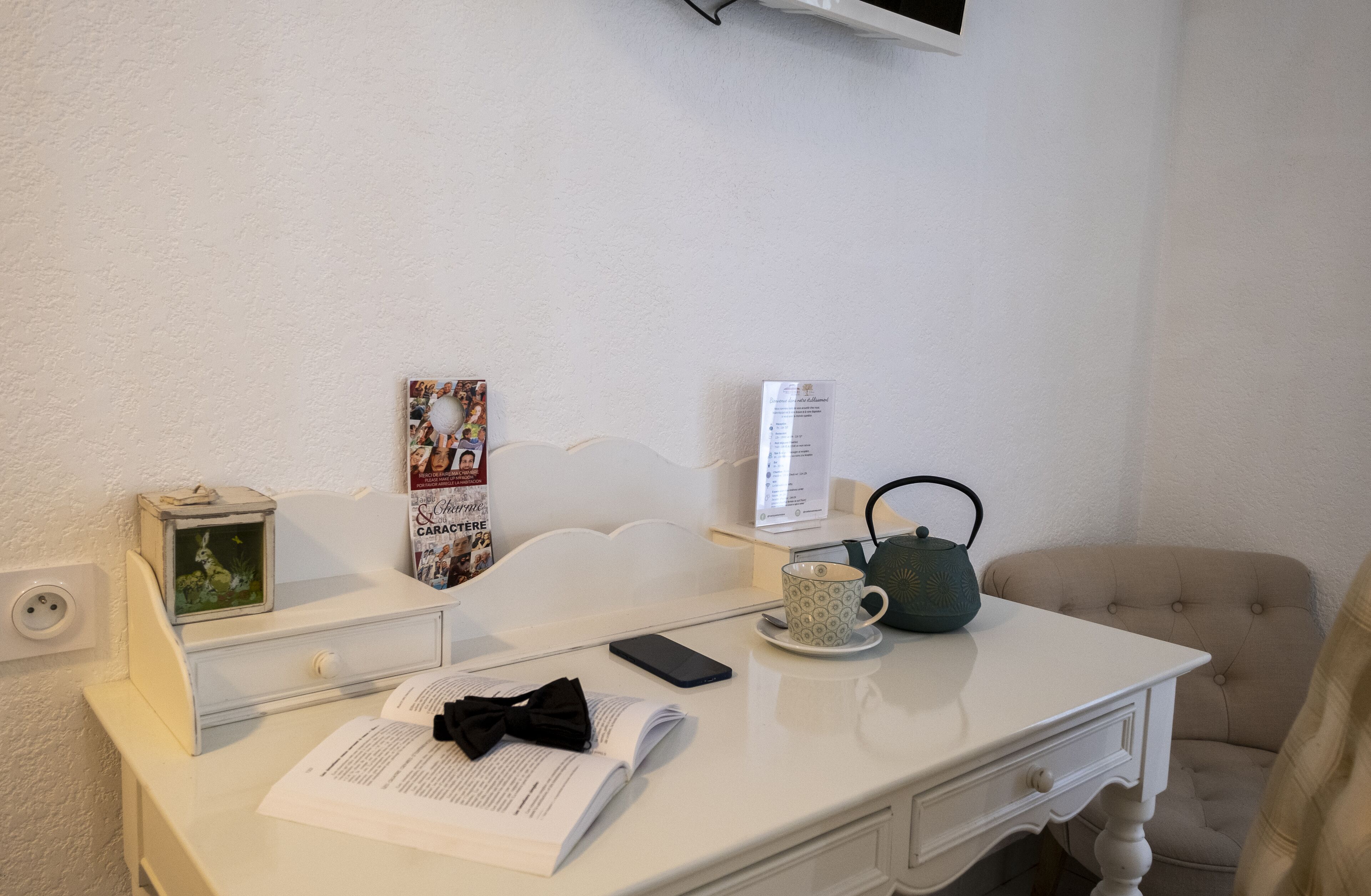 A neatly arranged desk with a book, a mobile phone, a teapot, a cup, a clock, and a poster.