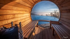 Een houten interieur met een rond raam dat uitzicht biedt op een meer en bomen.